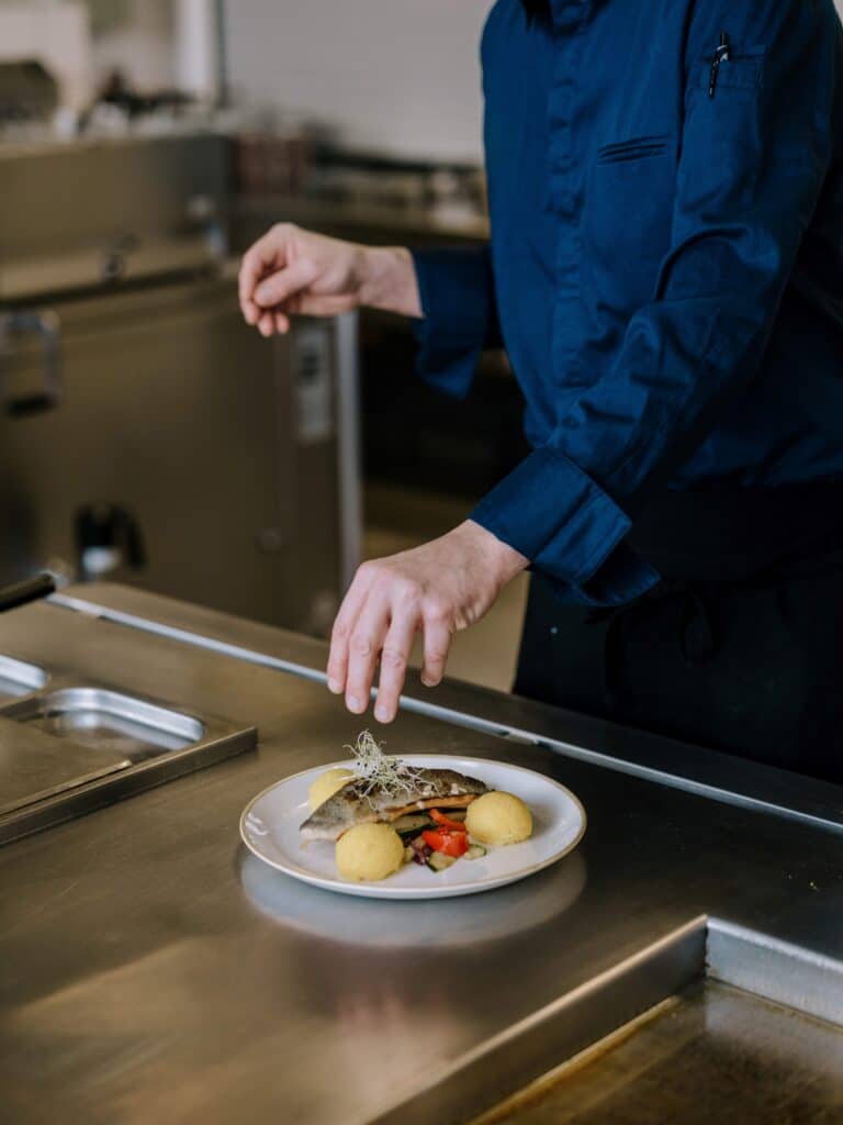 Anrichten eines warmen Hauptgerichts mit Fisch, Knödeln und Gemüse in einer Profiküche